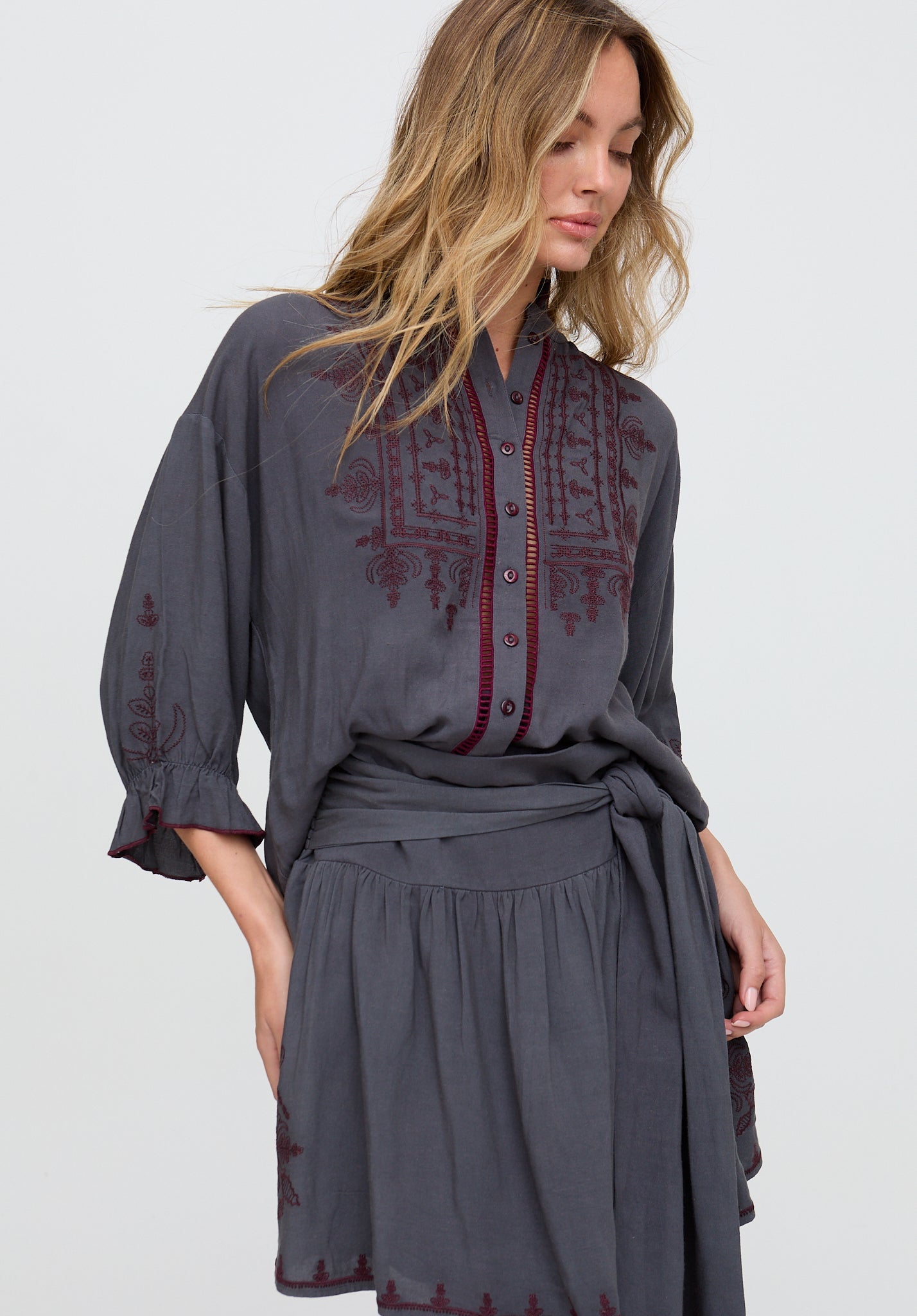 Woman wearing a gray dress with red embroidery on a white background