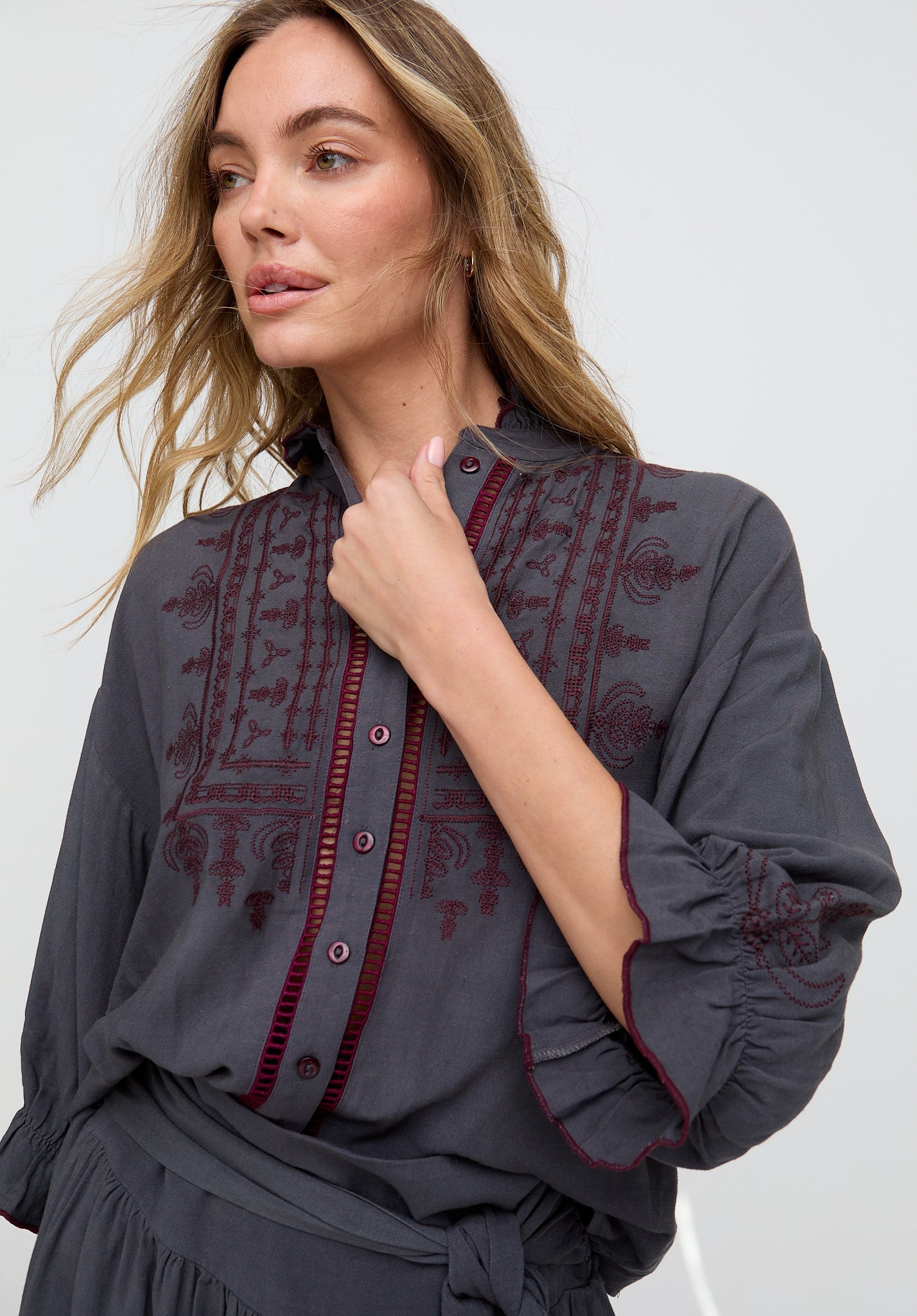 Woman wearing a dark gray blouse with red embroidery on a white background