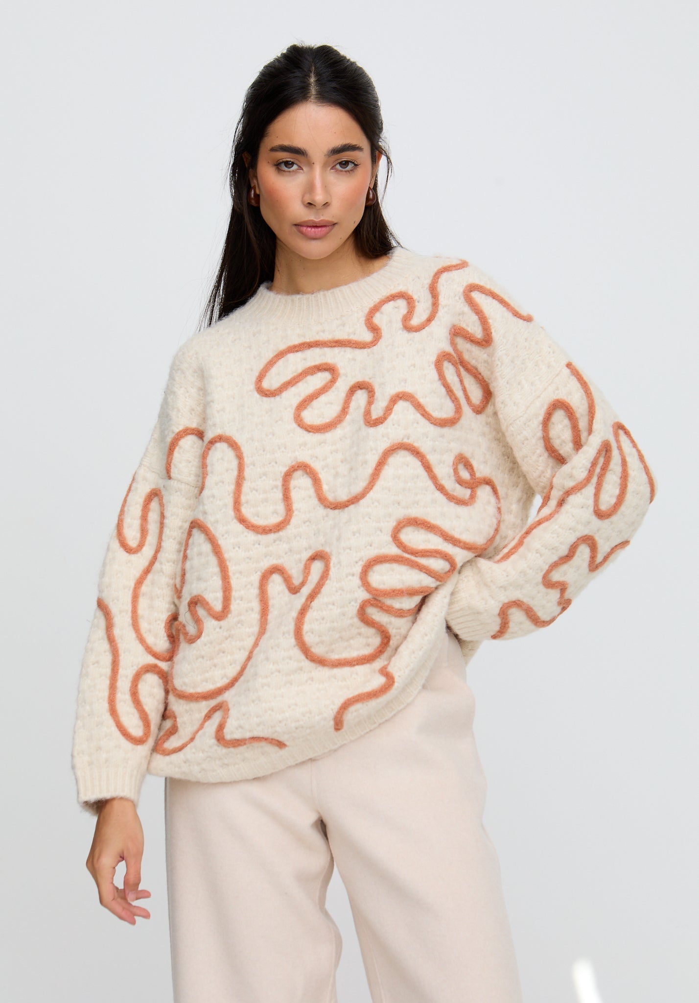 Woman wearing a cream sweater with orange abstract patterns on a plain background