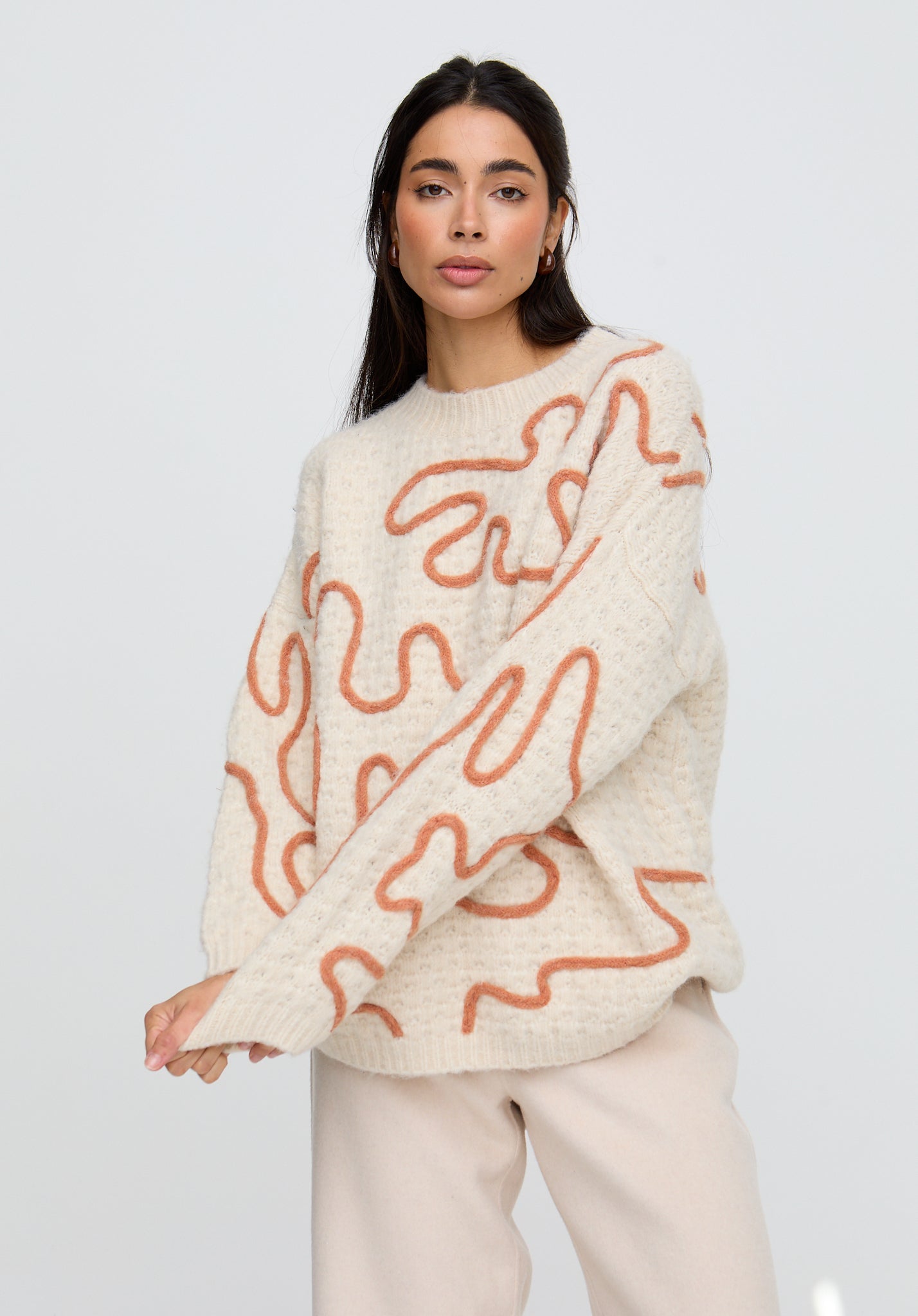 Woman wearing a cream sweater with orange abstract patterns on a plain background