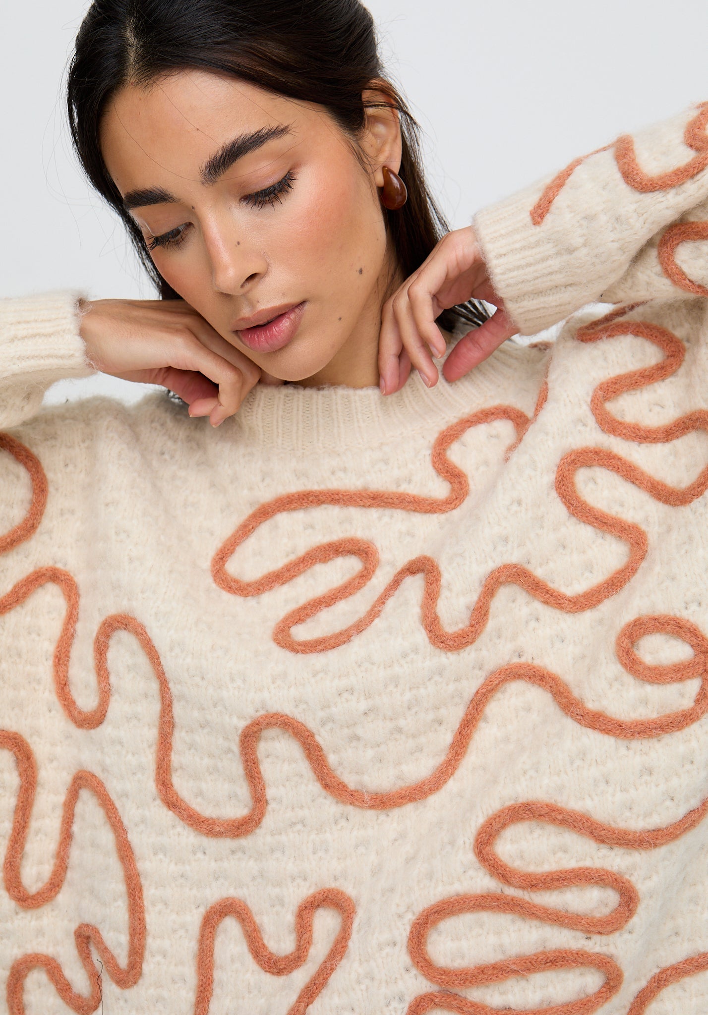 Woman wearing a cream sweater with orange abstract patterns against a white background
