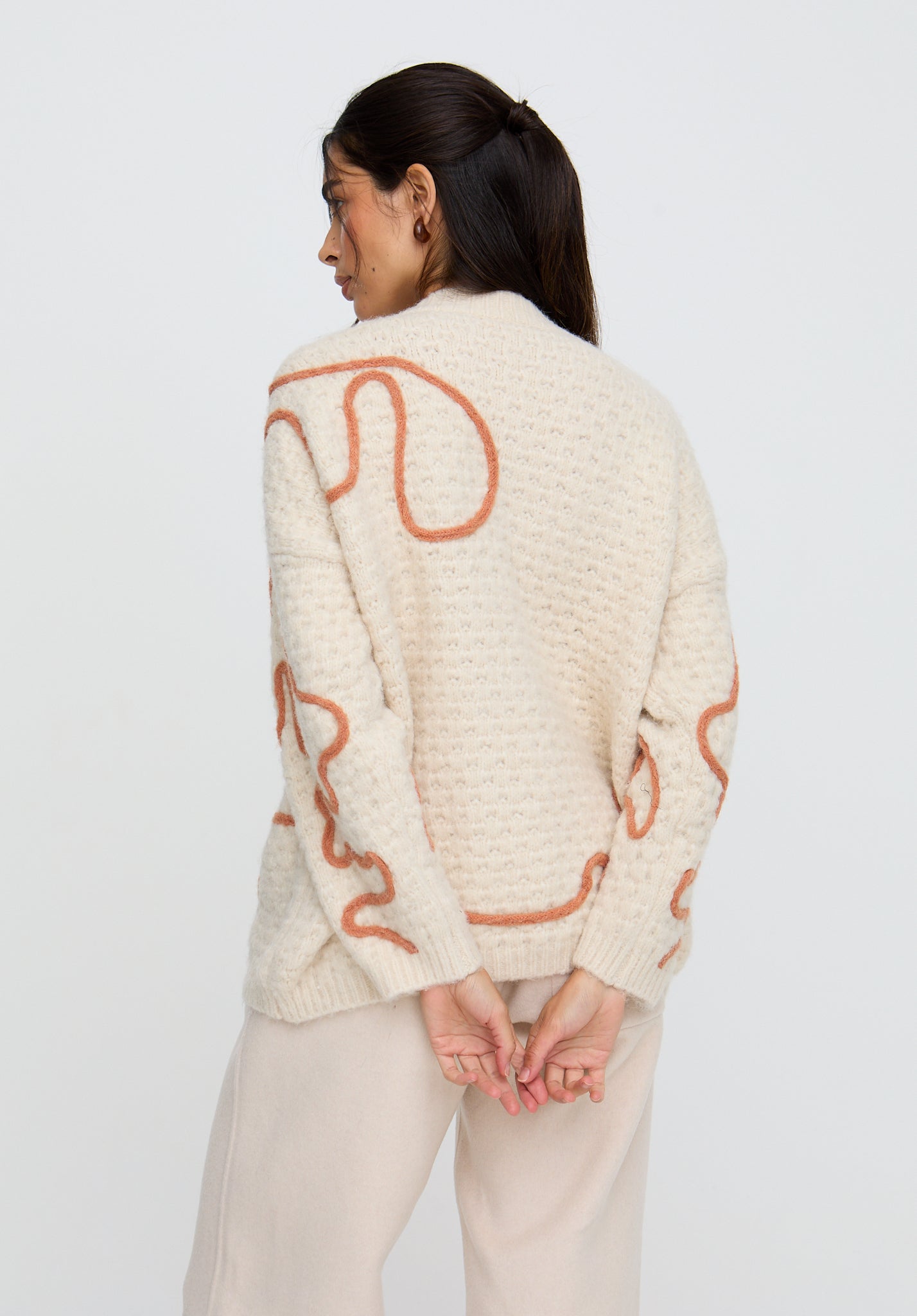 Woman wearing a cream sweater with orange abstract patterns on a white background