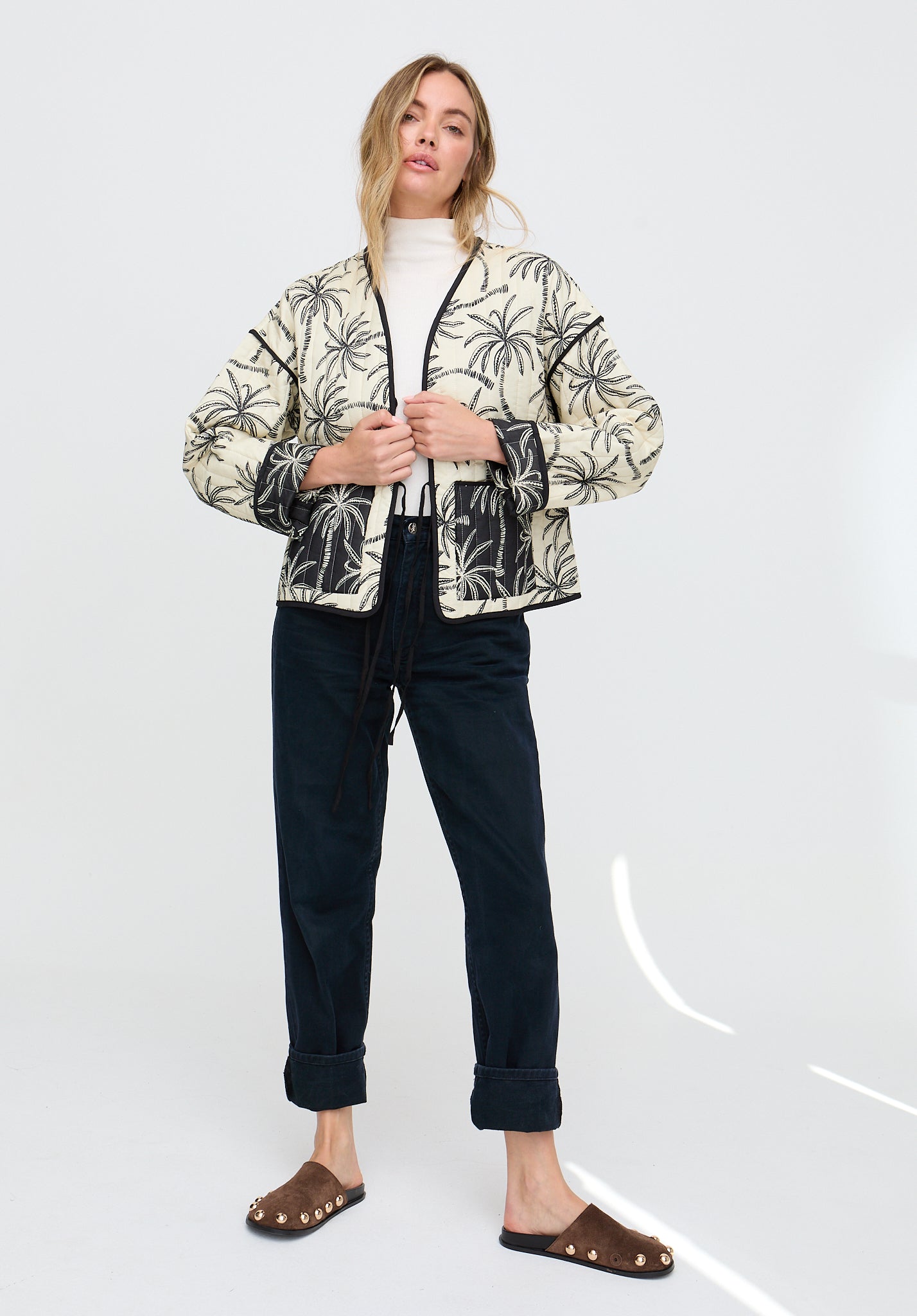 Woman wearing a patterned jacket and dark pants on a white background