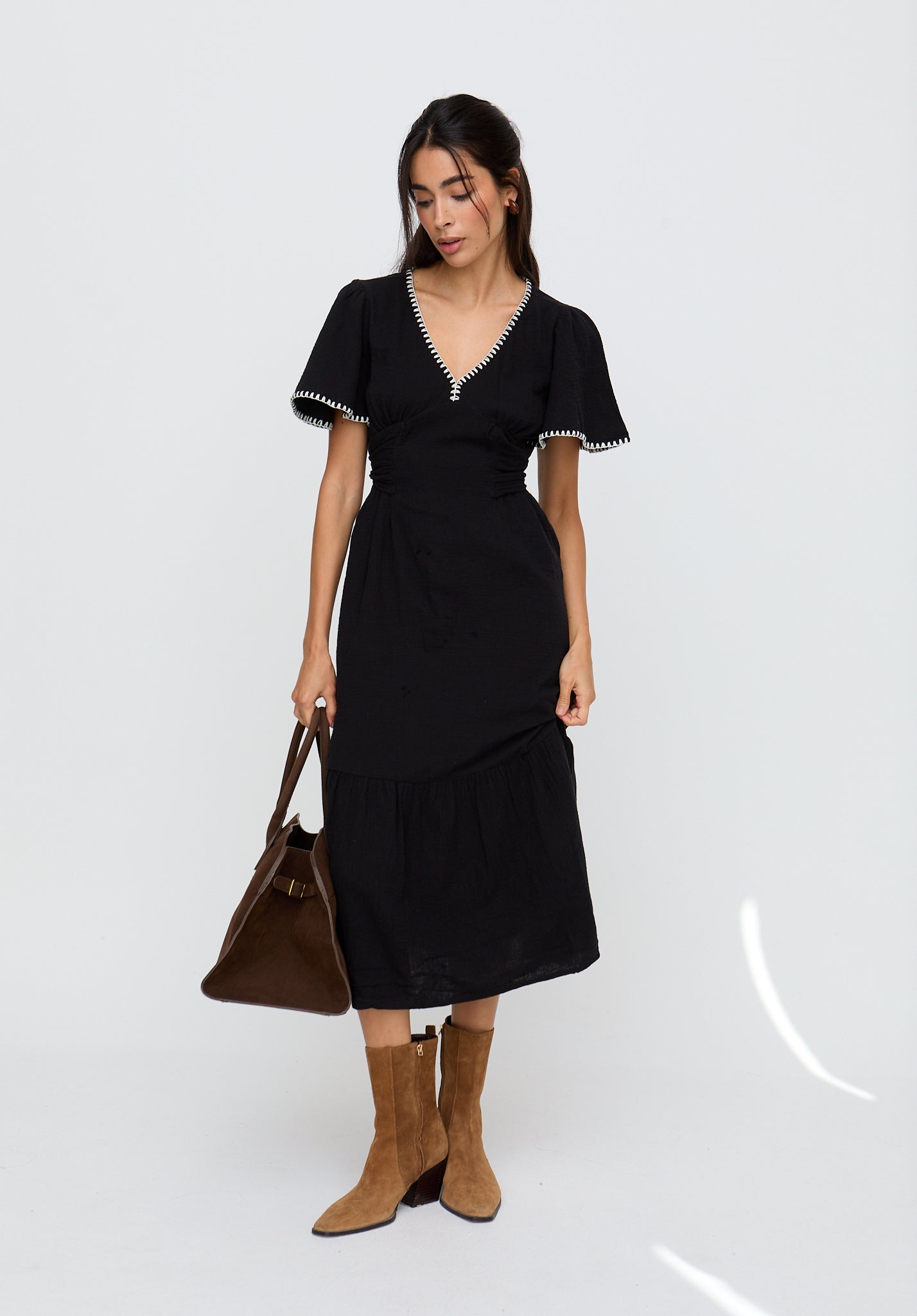 Woman wearing a black dress with white trim, holding a brown handbag on a white background