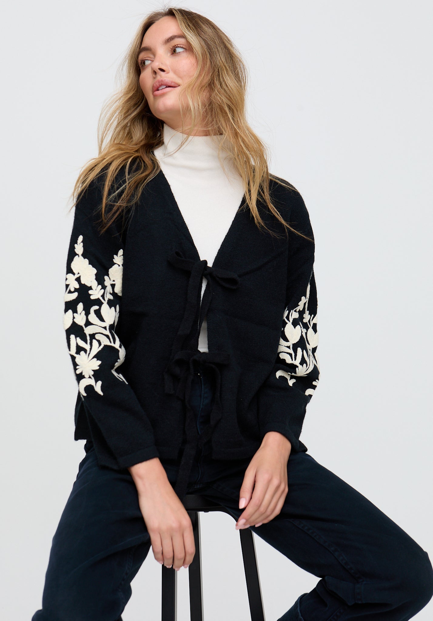 Woman wearing a black cardigan with floral patterns on a white background