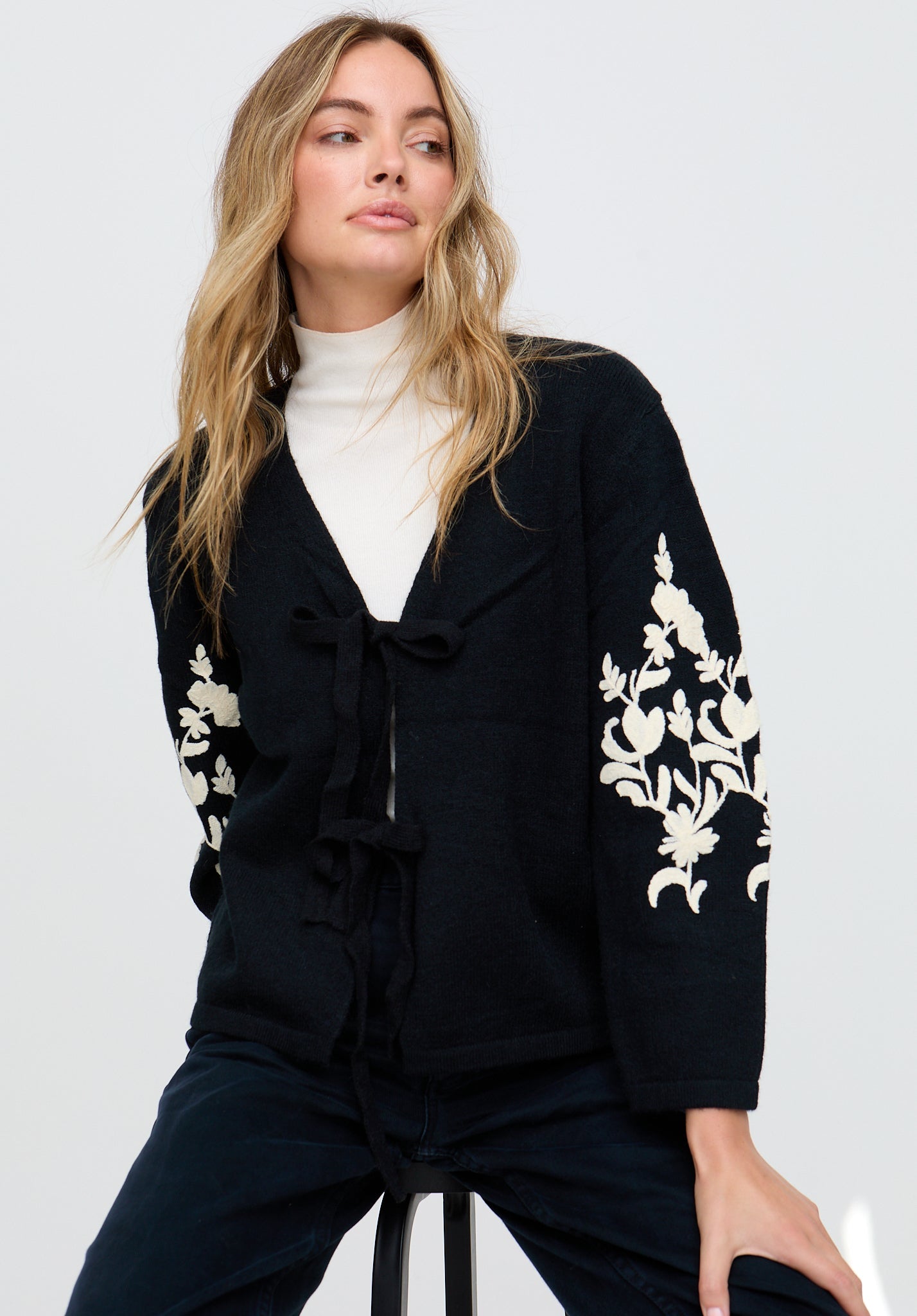 Woman wearing a black cardigan with white floral embroidery on a white background