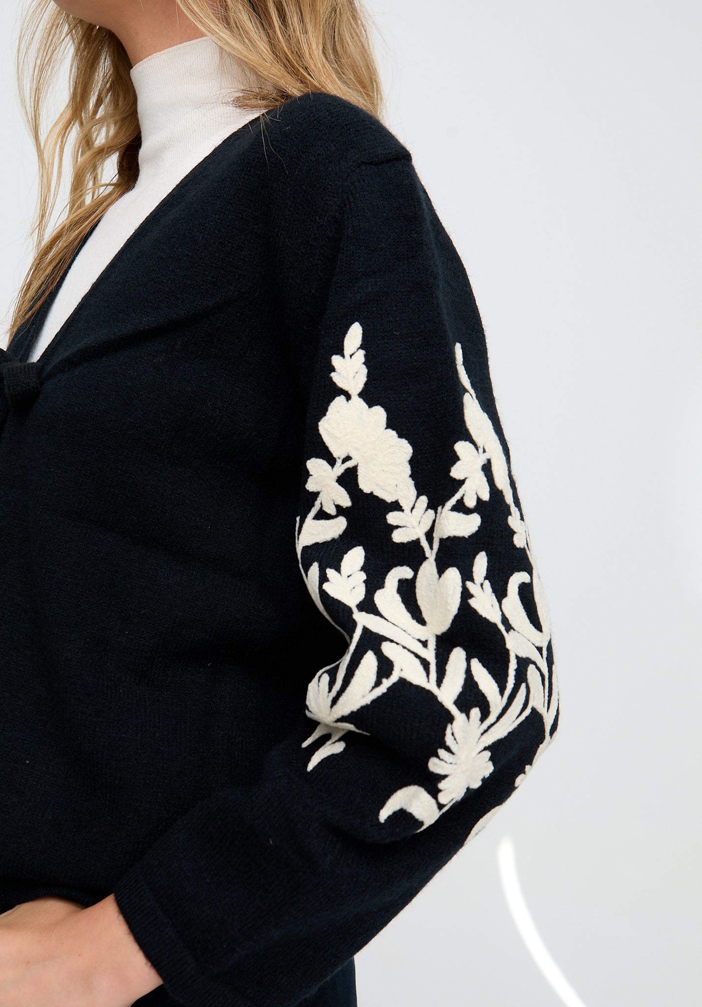 Black cardigan with white floral patterns on sleeves against a white background