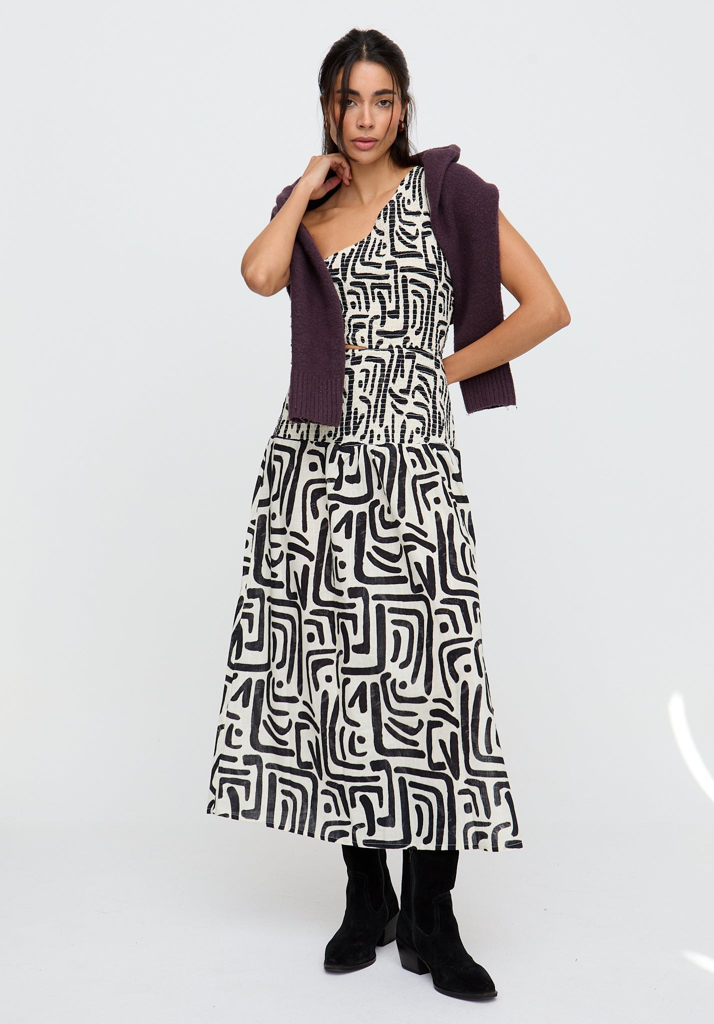 Woman wearing a black and white patterned dress with a purple cardigan on a white background