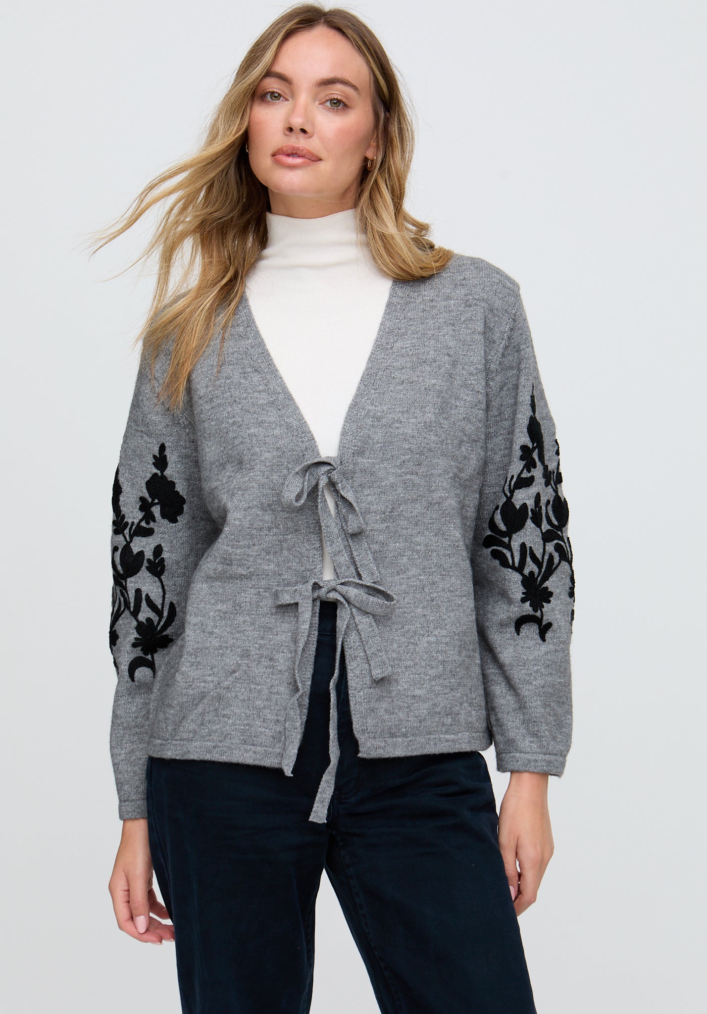 Woman wearing a gray cardigan with black floral embroidery on a white background