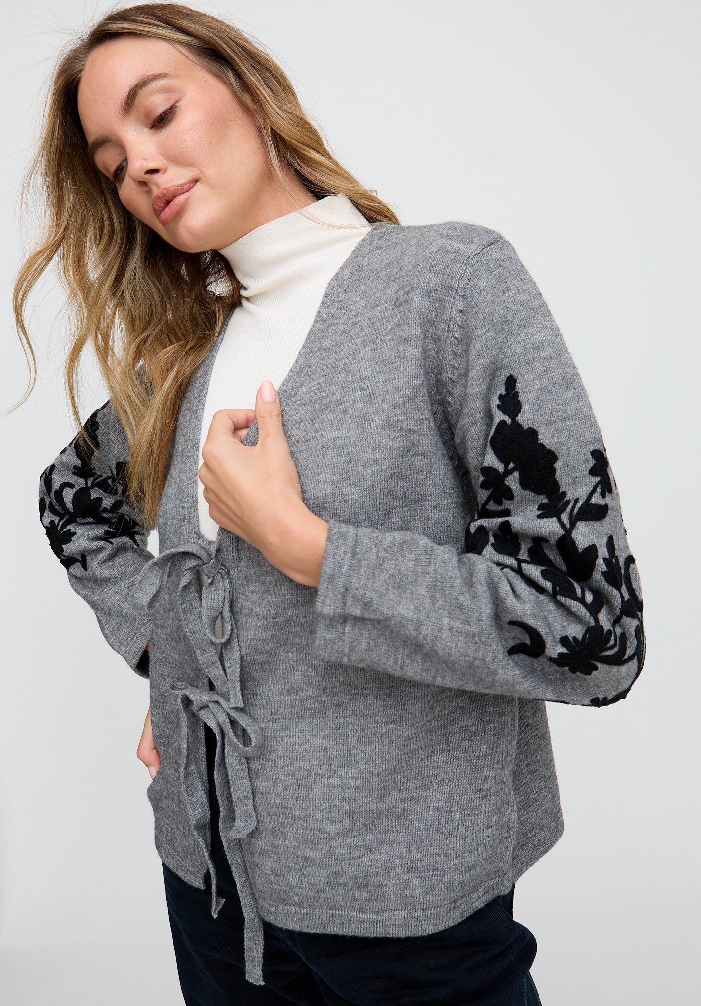 Woman wearing a gray cardigan with floral sleeves on a white background
