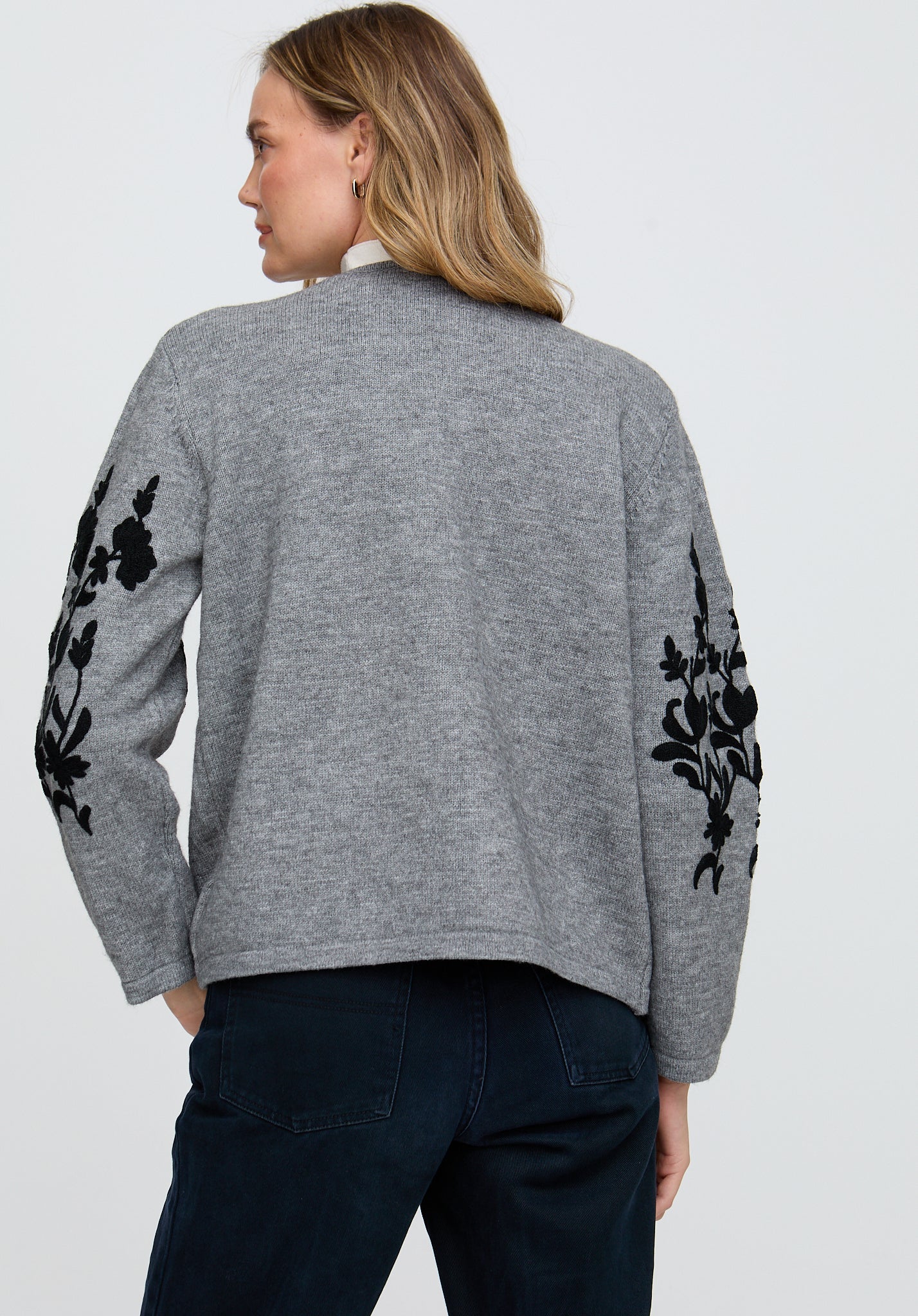 Woman wearing a gray sweater with black floral patterns on sleeves against a white background