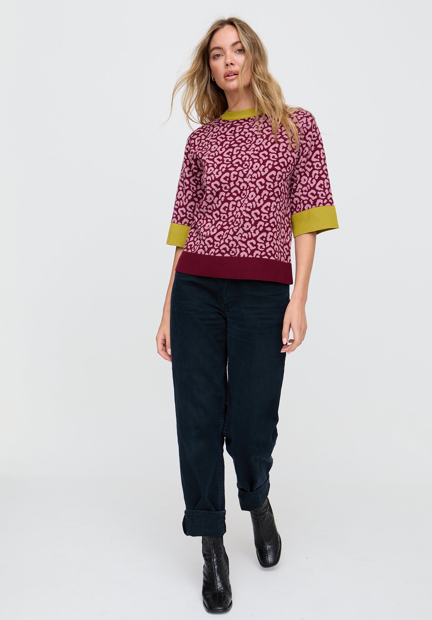 Woman wearing a patterned top and dark pants on a white background