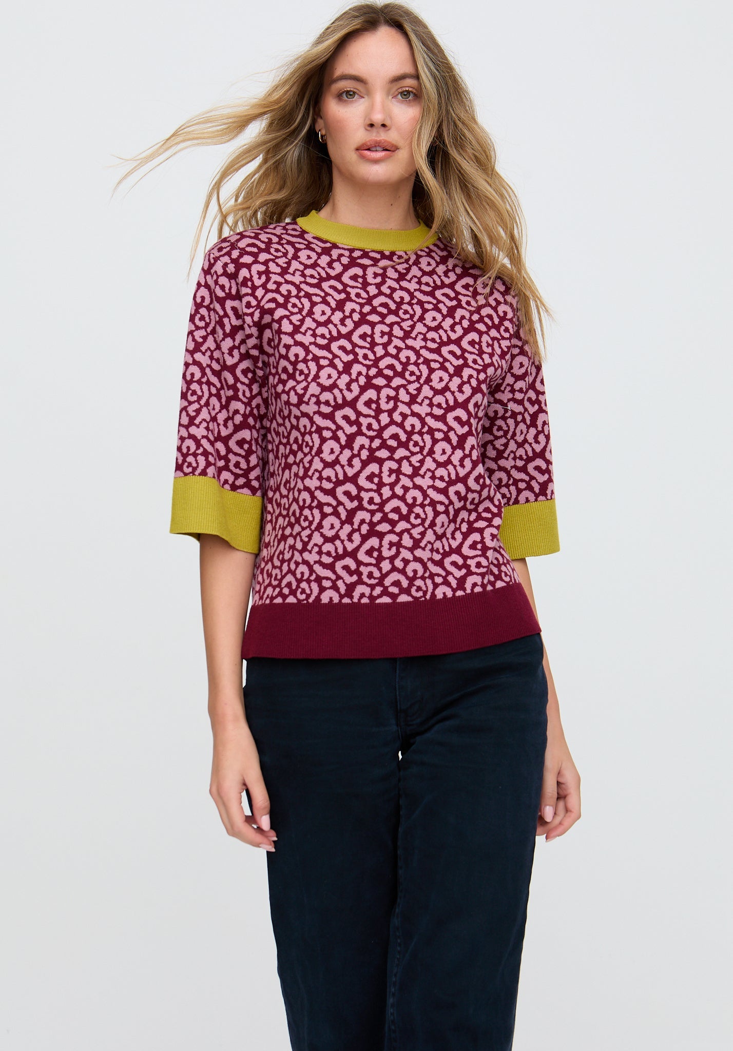 Woman wearing a pink leopard print sweater with green accents on a white background