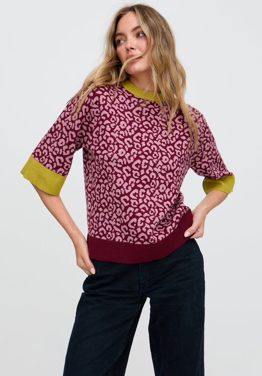 Woman wearing a pink leopard print sweater with green cuffs and hem on a white background