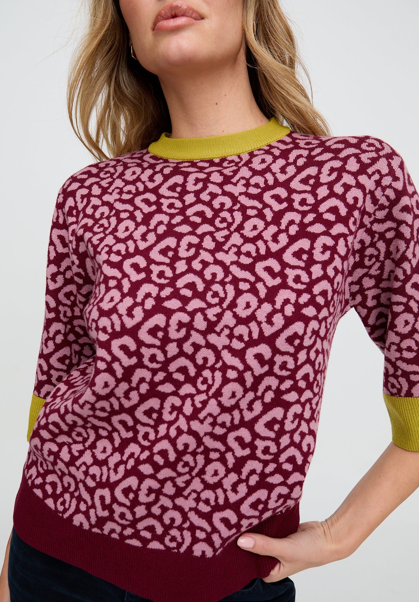 Person wearing a pink leopard print sweater with green accents on a white background