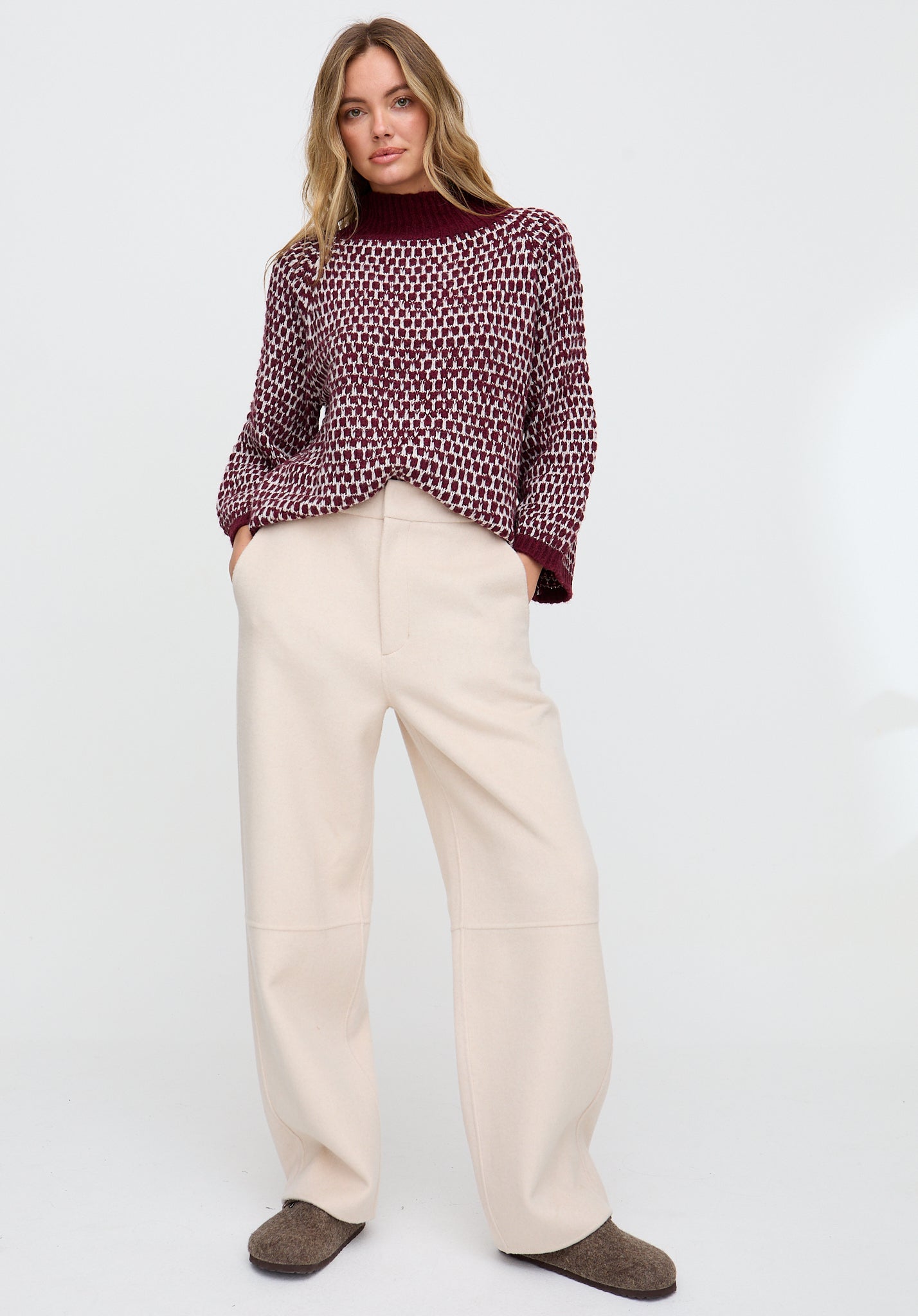 Woman wearing a patterned blouse and beige pants on a white background