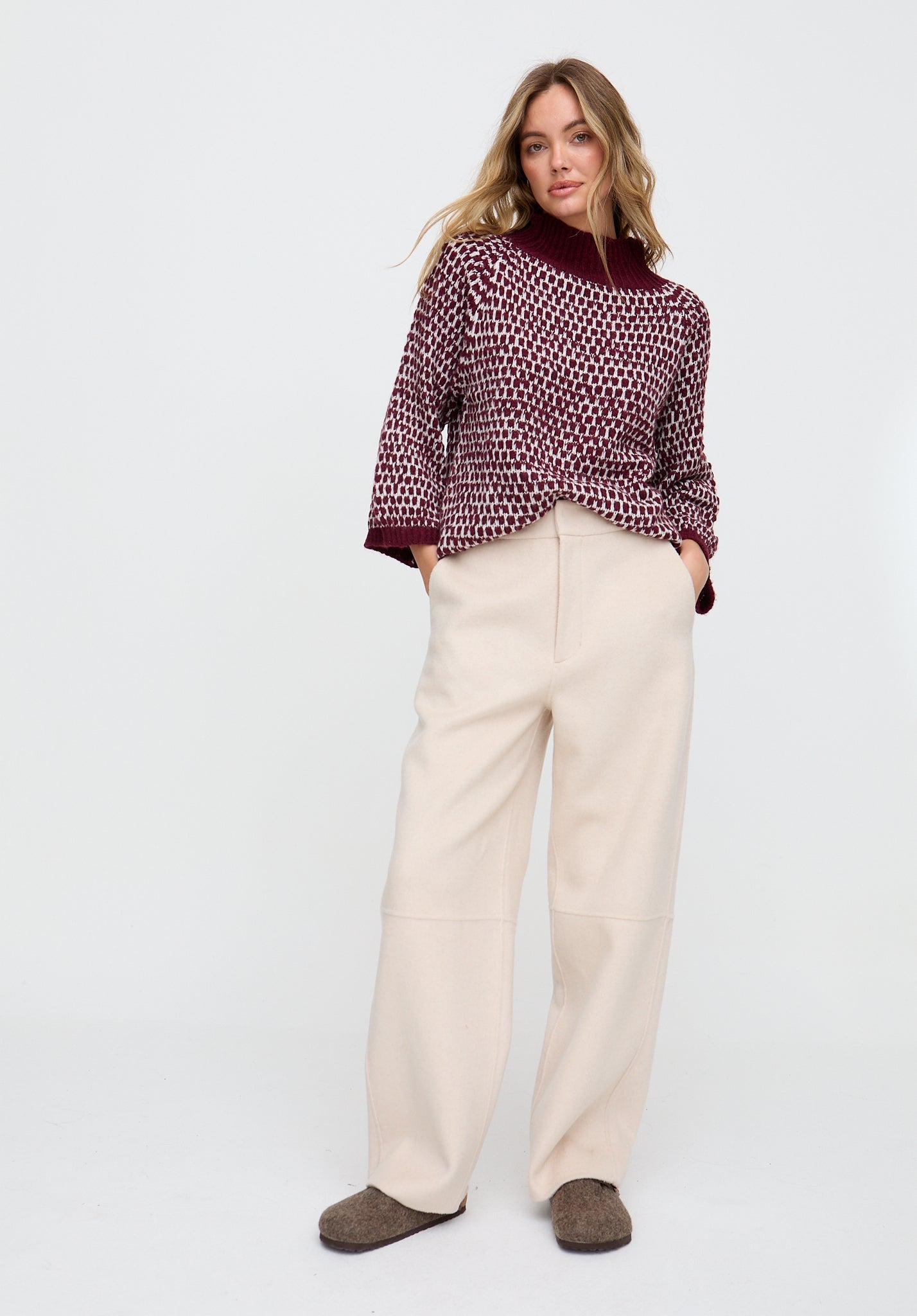 Woman wearing a patterned top and beige pants on a white background