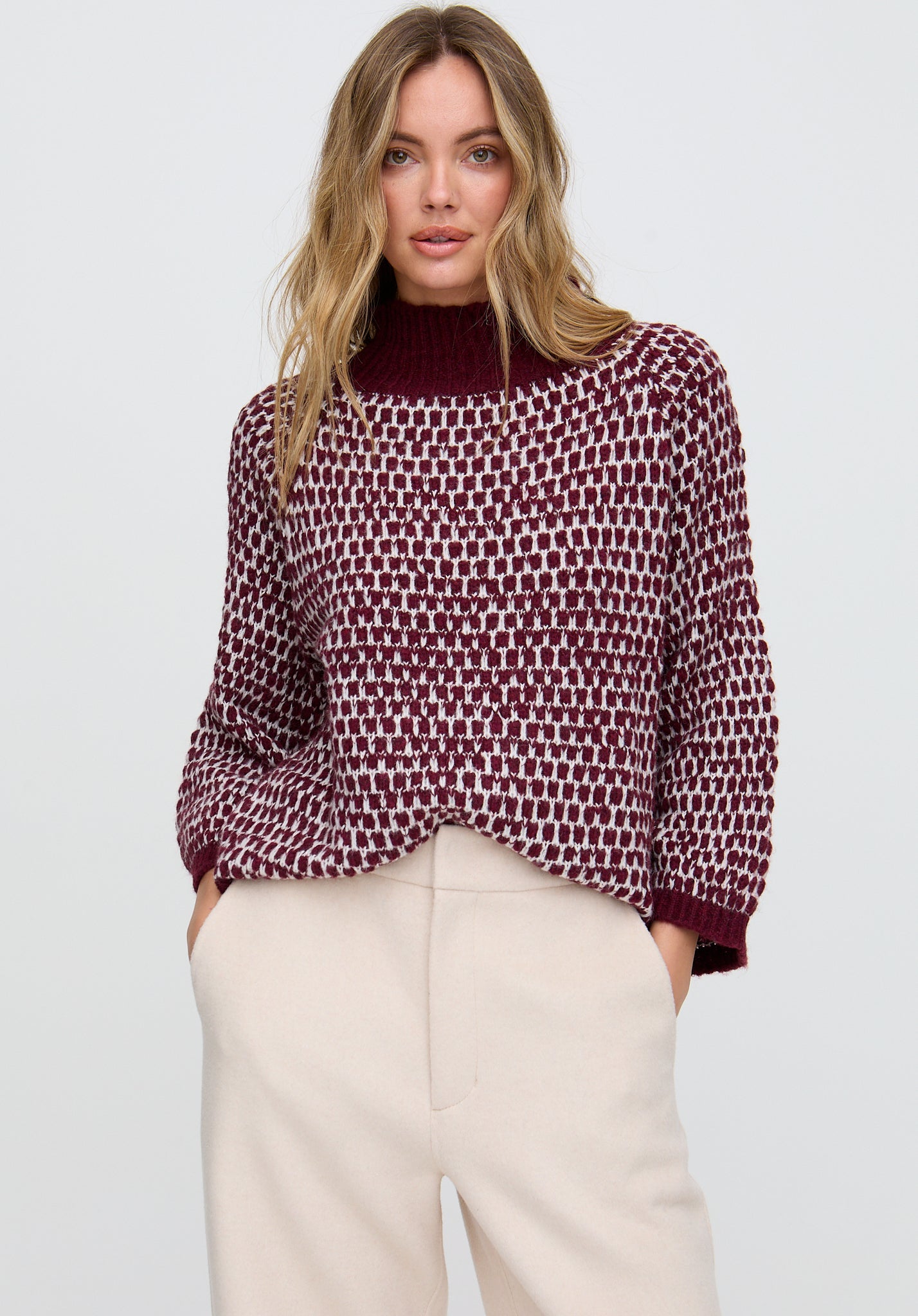 Woman wearing a patterned sweater and beige pants against a plain background