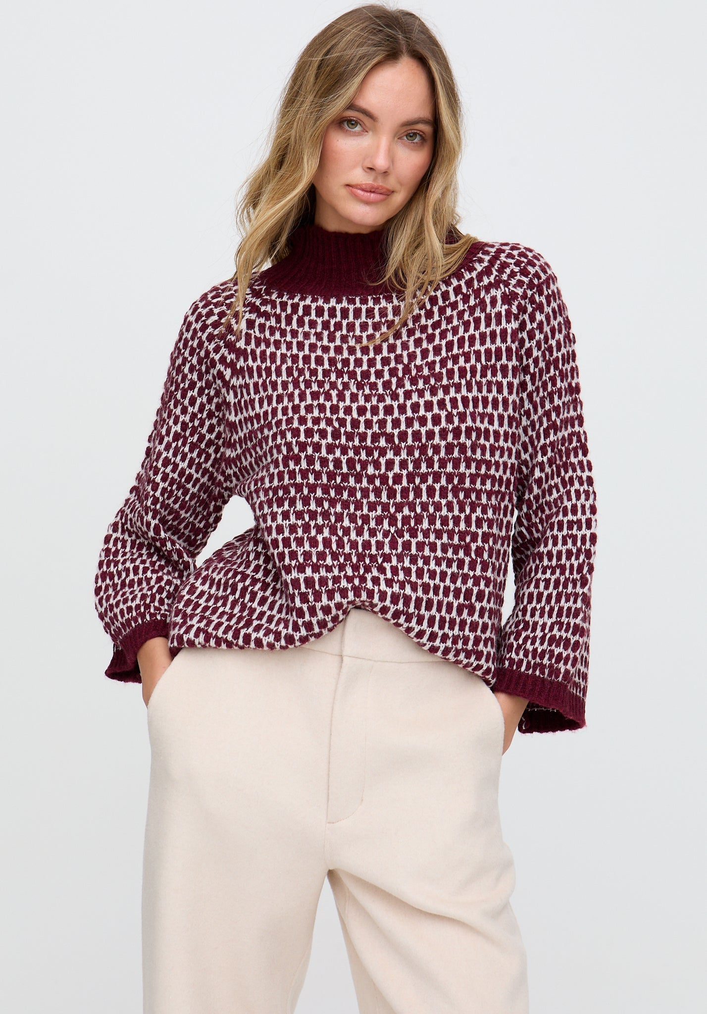 Woman wearing a patterned blouse and beige pants on a plain background