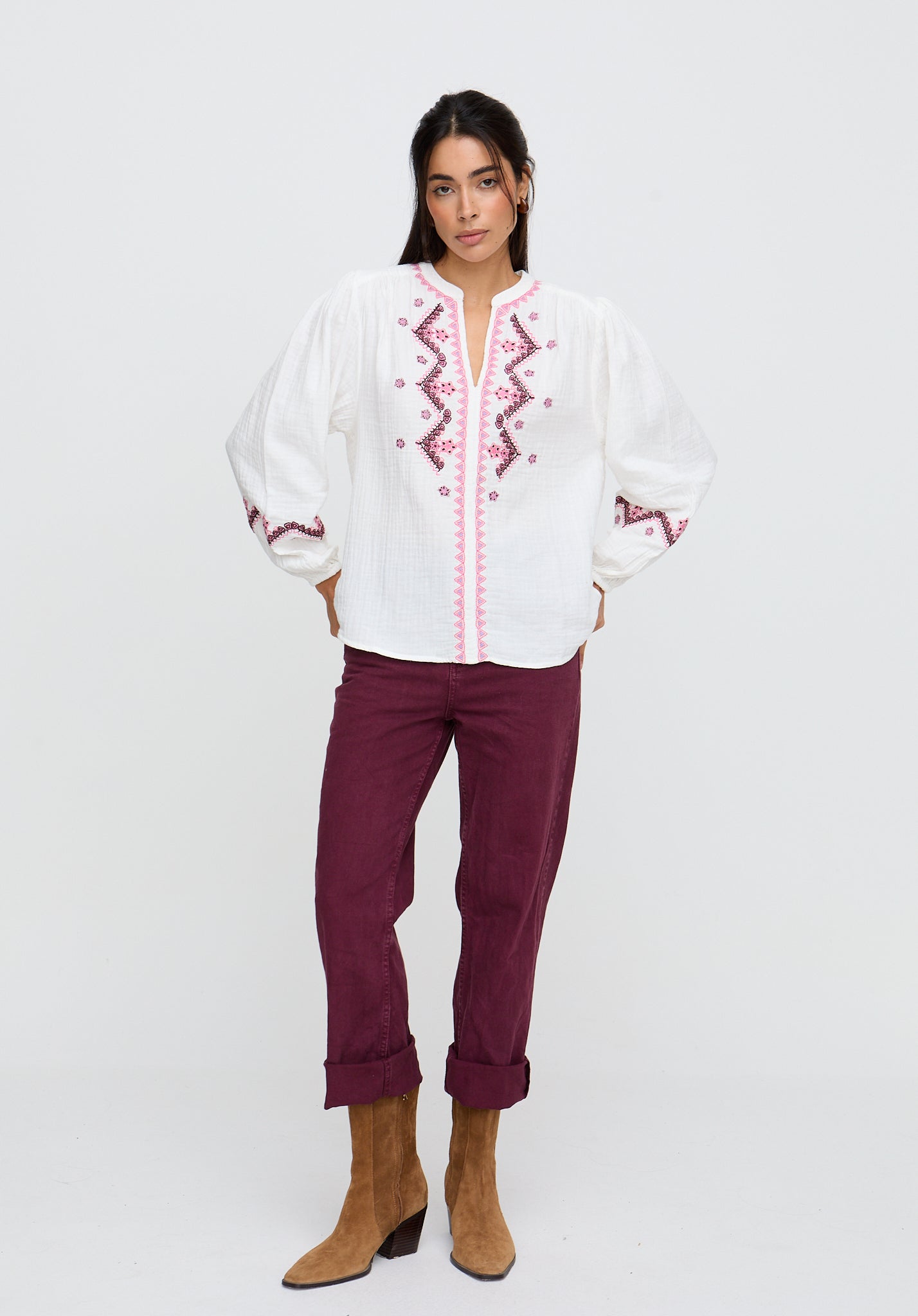 Woman wearing a white blouse with red embroidery and purple pants on a white background