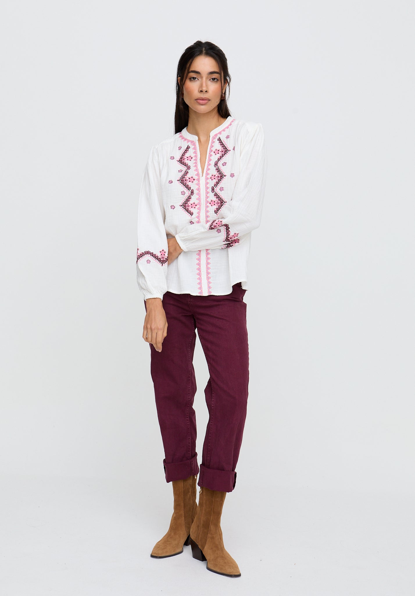 Woman wearing a white blouse with red embroidery and burgundy pants on a white background