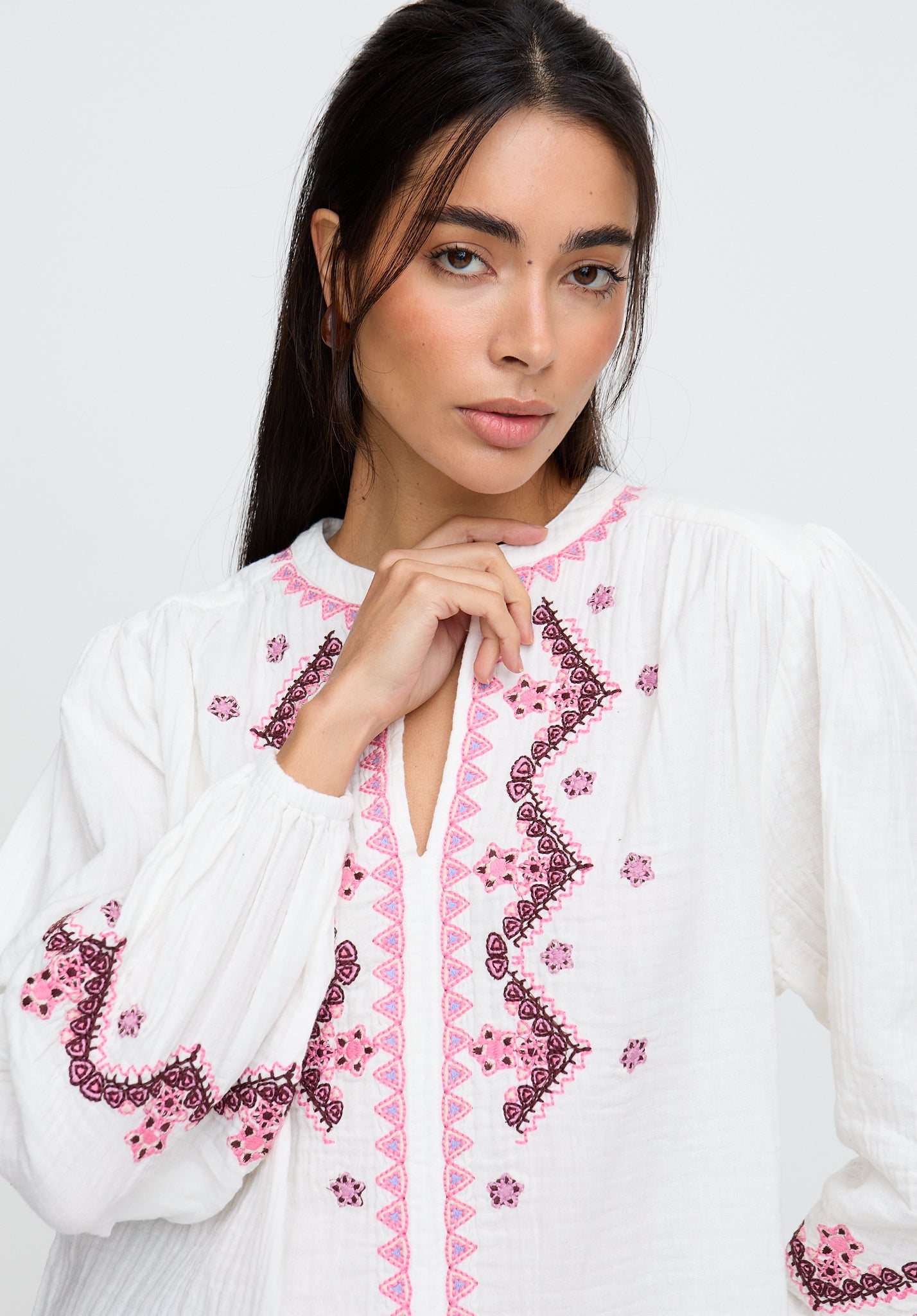 Woman wearing a white blouse with pink embroidery on a plain background
