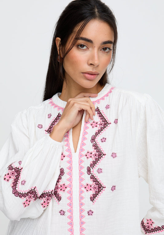 Woman wearing a white blouse with pink embroidery on a plain background