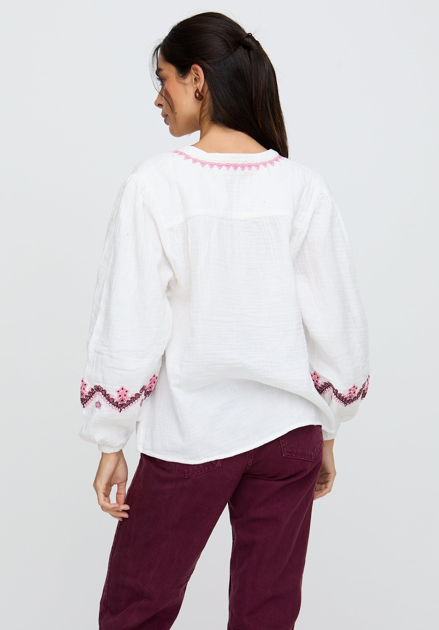 Woman wearing a white blouse with pink embroidery and maroon pants on a white background