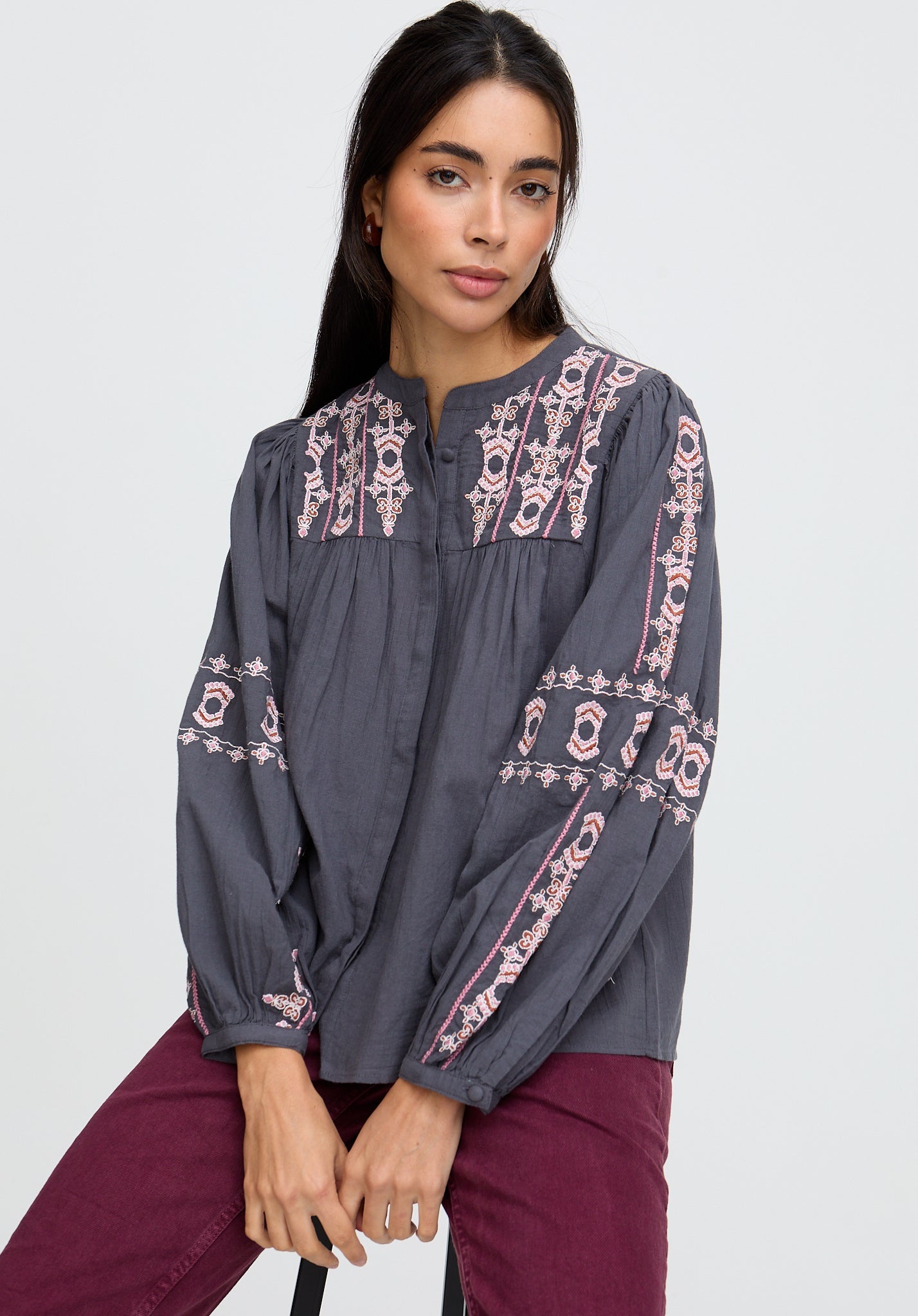 Woman wearing a gray blouse with intricate pink embroidery on a white background