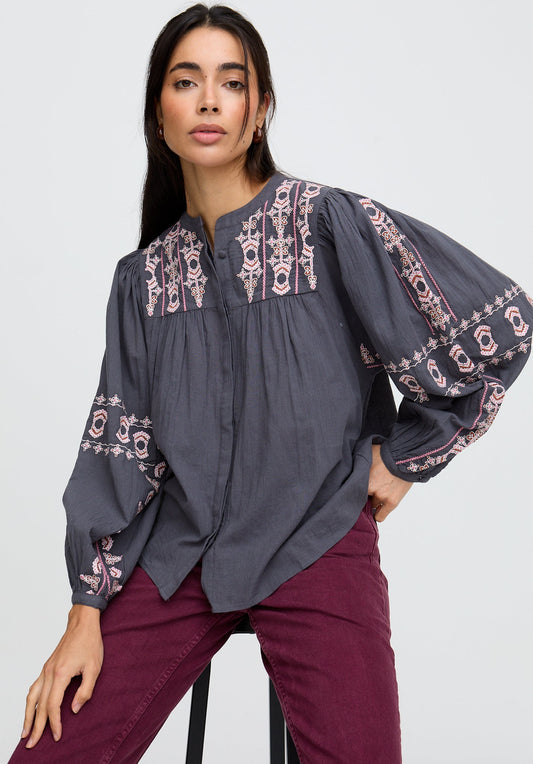 Woman wearing a dark gray blouse with pink embroidery on a white background