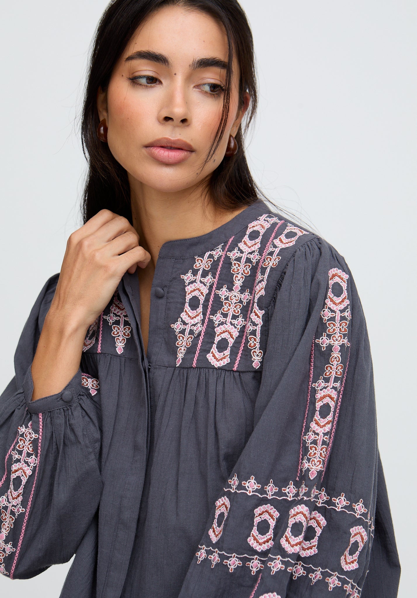 Woman wearing a dark gray embroidered blouse against a light background