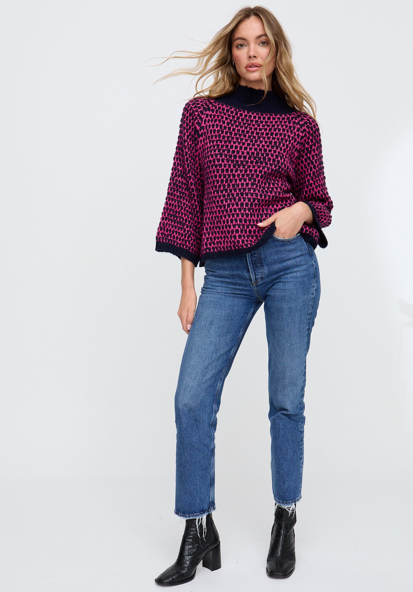 Woman wearing a patterned sweater, jeans, and black boots on a white background