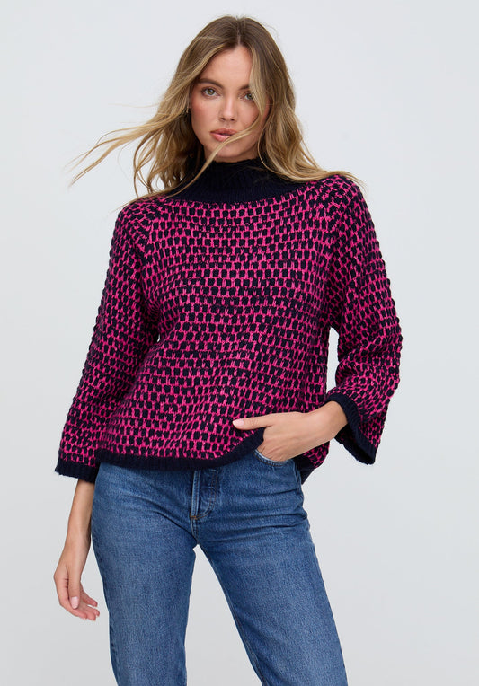Woman wearing a pink and black patterned sweater with blue jeans on a light gray background