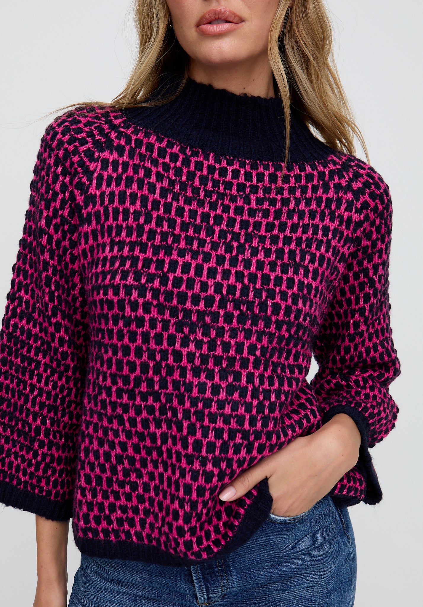Person wearing a pink and black patterned sweater with a plain background