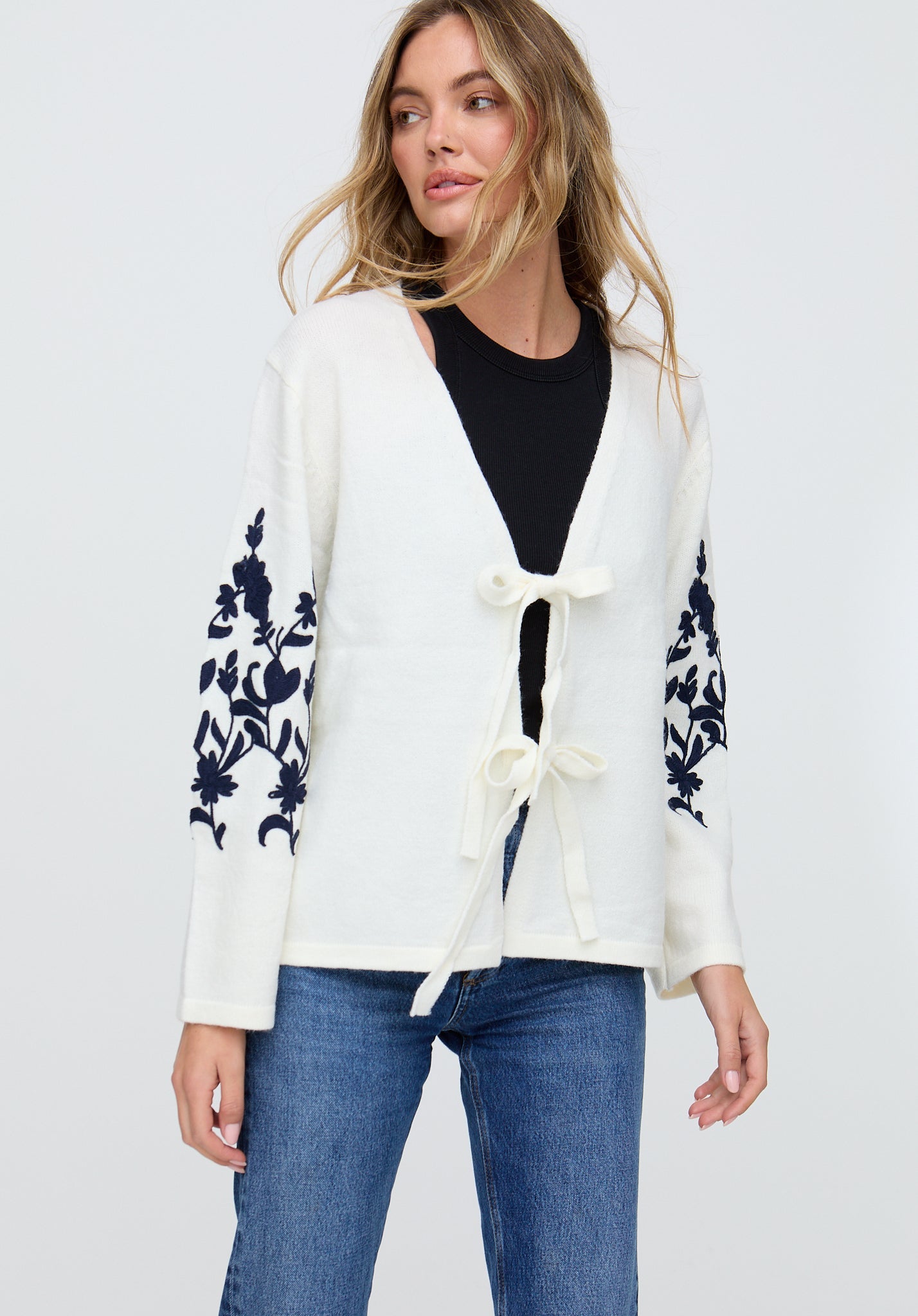 Woman wearing a white cardigan with floral patterns on sleeves against a plain background