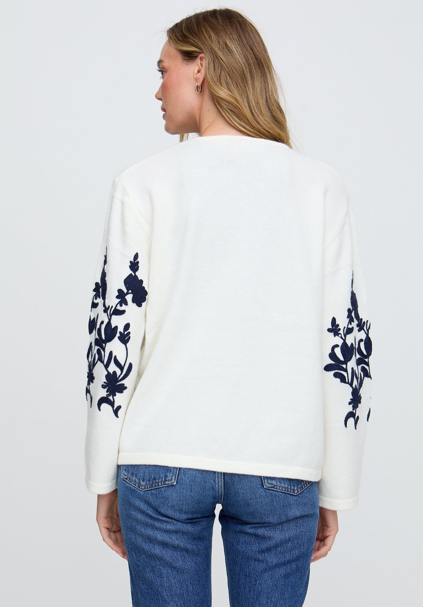 Woman wearing a white sweater with blue floral patterns on a plain background
