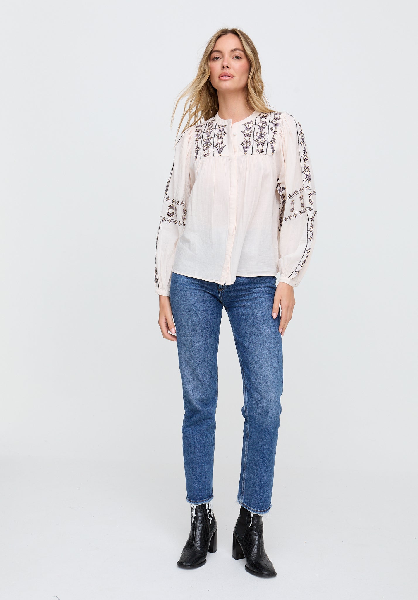Woman wearing a white blouse with embroidery and blue jeans on a white background