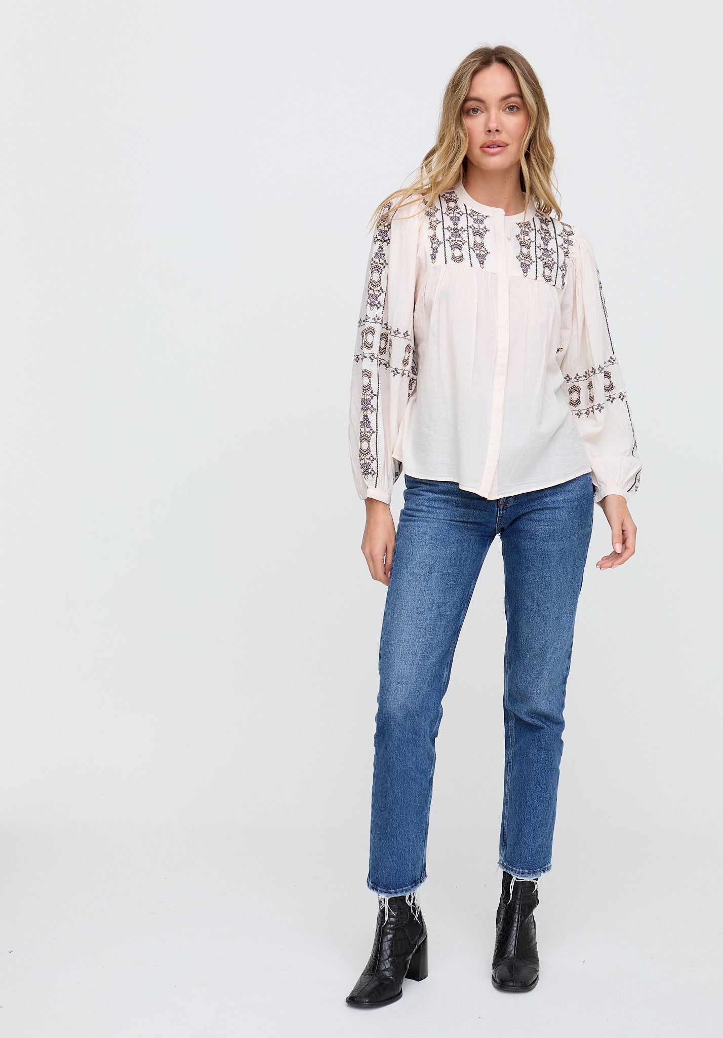 Woman wearing a white blouse with embroidery and blue jeans on a white background