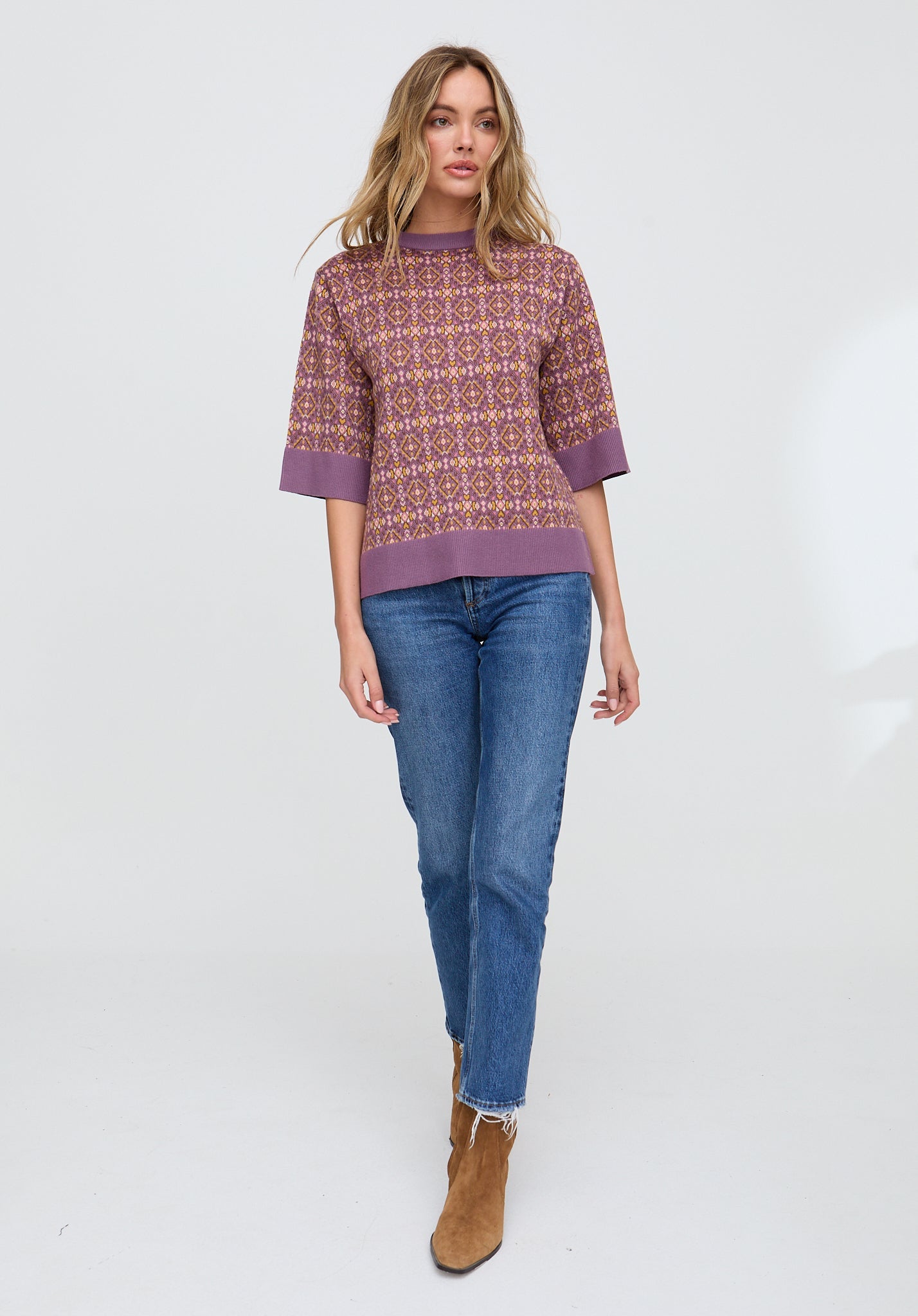 Woman wearing a patterned sweater and blue jeans on a white background