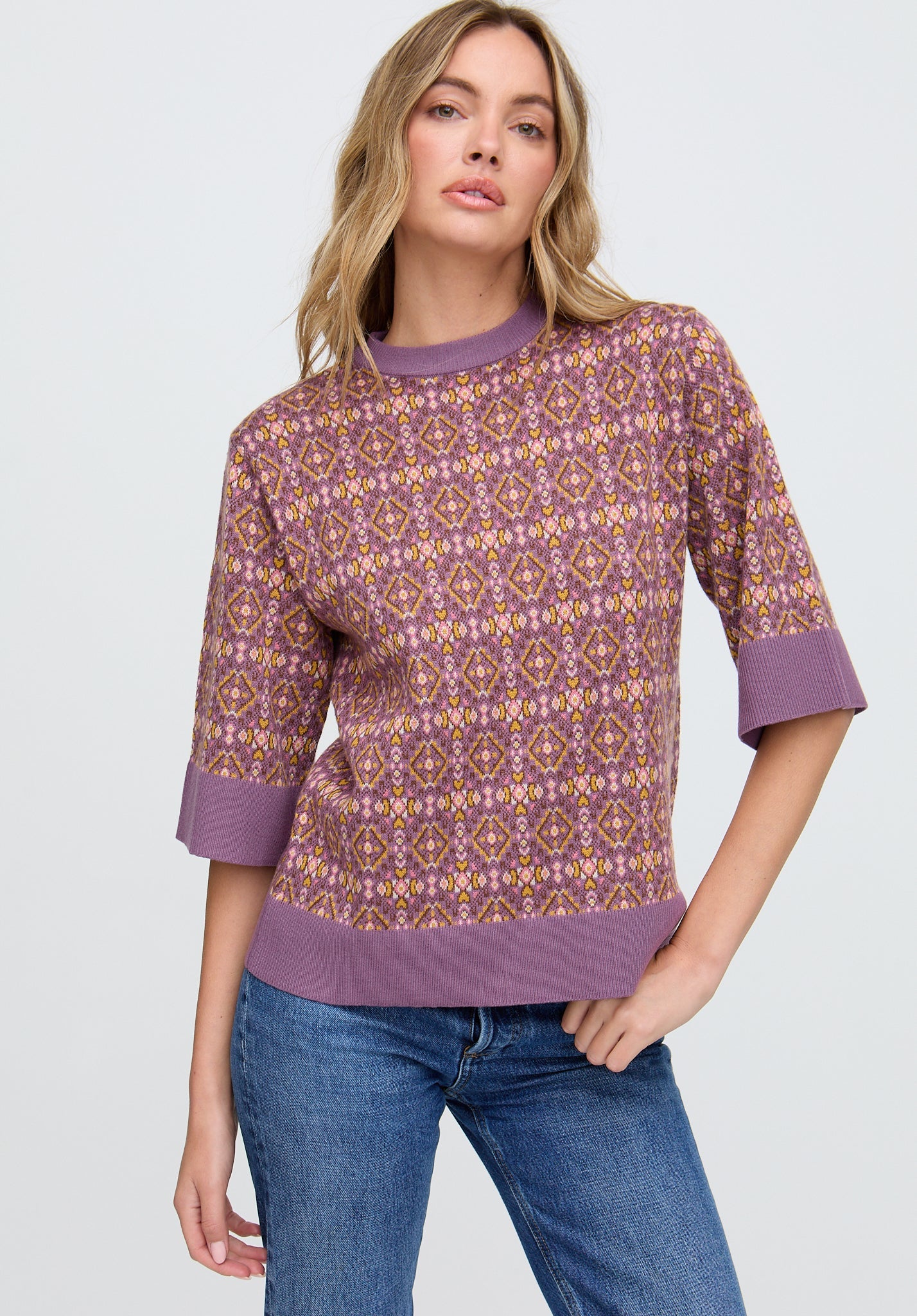 Woman wearing a patterned purple sweater and blue jeans on a white background