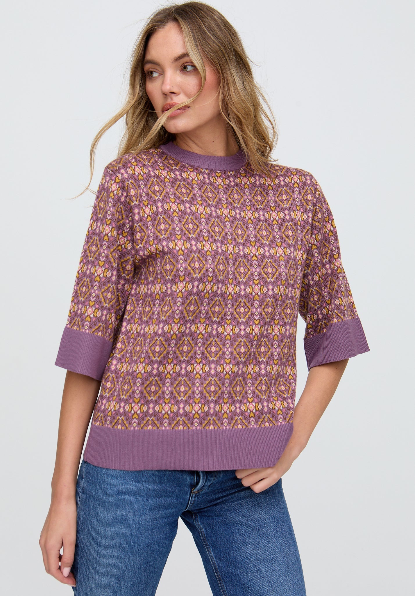 Woman wearing a patterned purple sweater and blue jeans on a white background