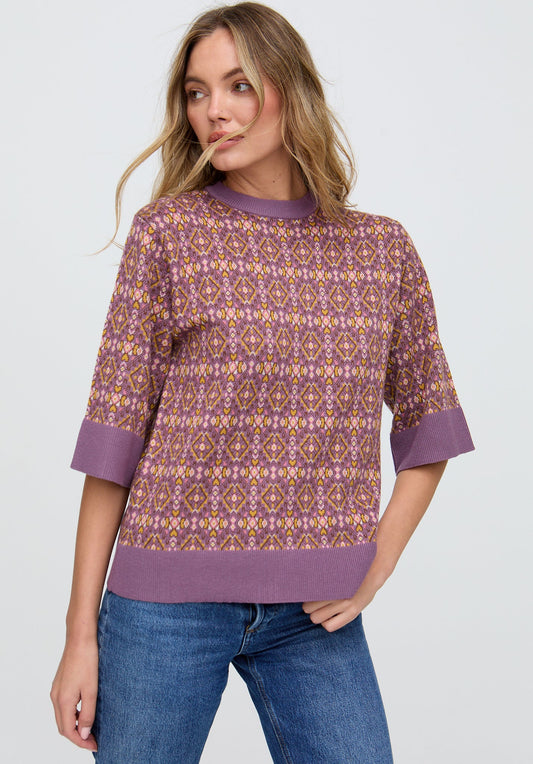 Woman wearing a patterned purple sweater and blue jeans on a white background