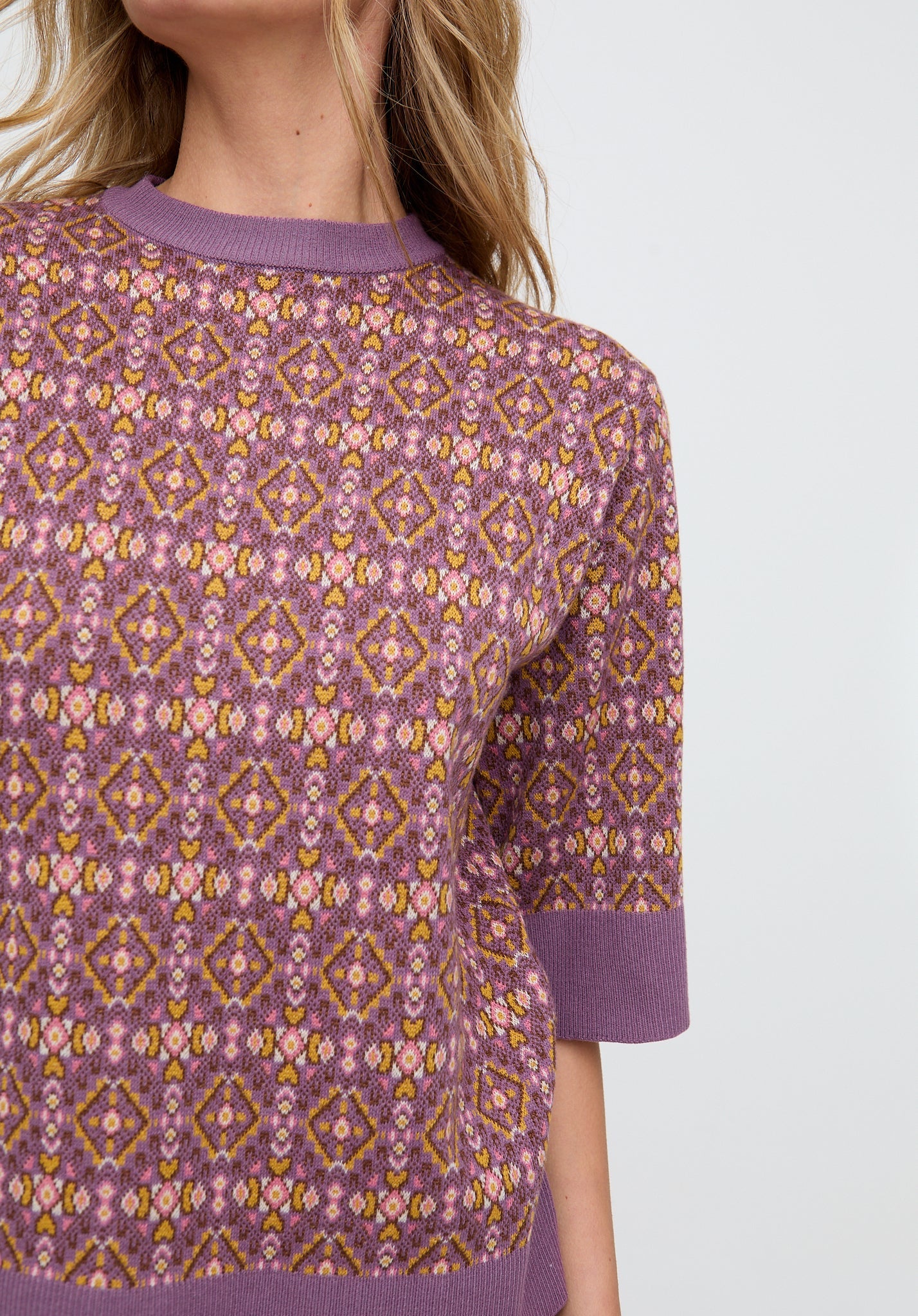 Purple patterned sweater worn by a person on a light gray background