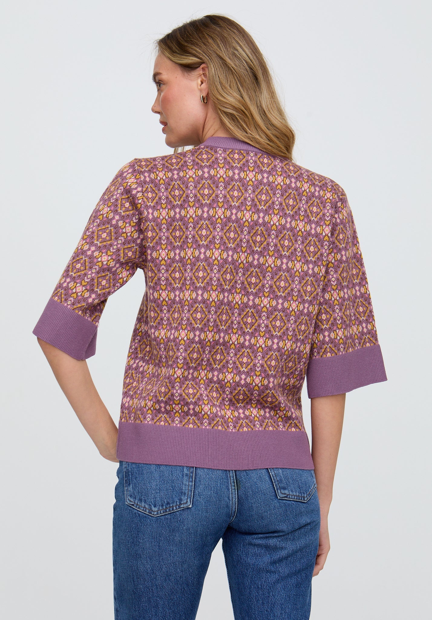 Woman wearing a patterned shirt with purple accents and blue jeans on a light gray background